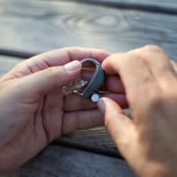Close up of someone holding their hearing aids at a table, troubleshooting feedback issues.