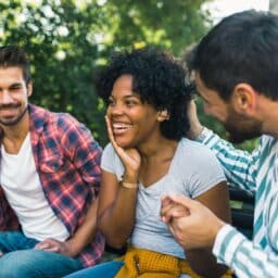 Smiling group of friends hanging out outside. One person wears hearing aids.