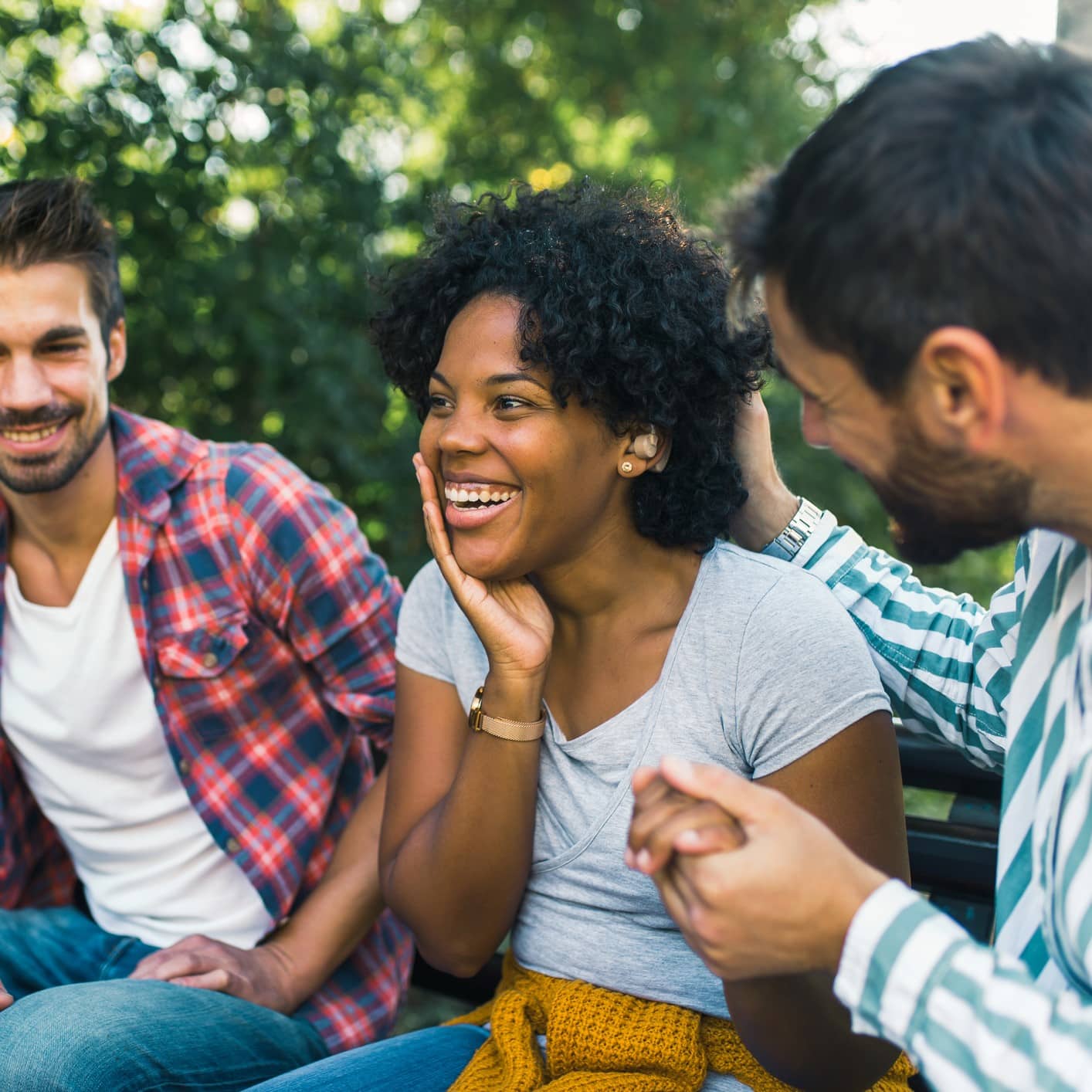 Smiling group of friends hanging out outside. One person wears hearing aids.