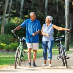 Happy couple walk their bikes together in a lovely wooded park.