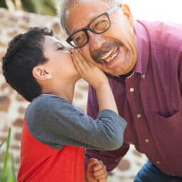 A joyful grandparent and his grandchild. The grandchild is whispering a secret in the grandparent's ear.