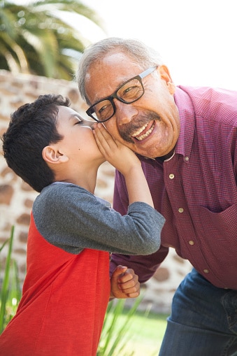 A joyful grandparent and his grandchild. The grandchild is whispering a secret in the grandparent's ear.