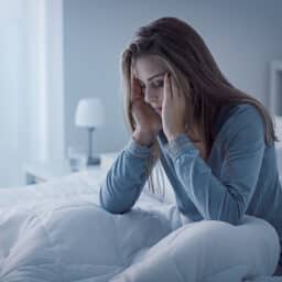 Tired woman in bed holds her forehead after a night of poor sleep. For some people, tinnitus is so severe that it affects and interrupts sleep.