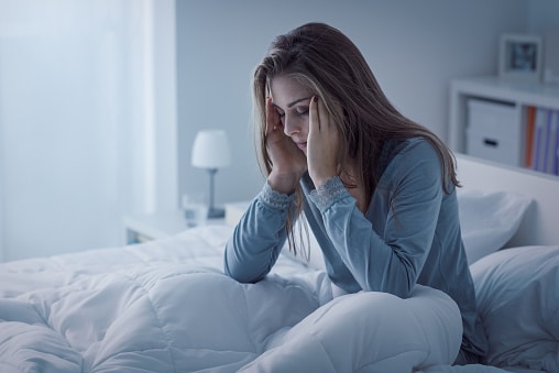 Tired woman in bed holds her forehead after a night of poor sleep. For some people, tinnitus is so severe that it affects and interrupts sleep.