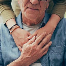 An older couple embraces with hands on the older man's chest.