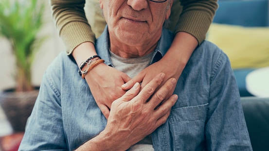 An older couple embraces with hands on the older man's chest.
